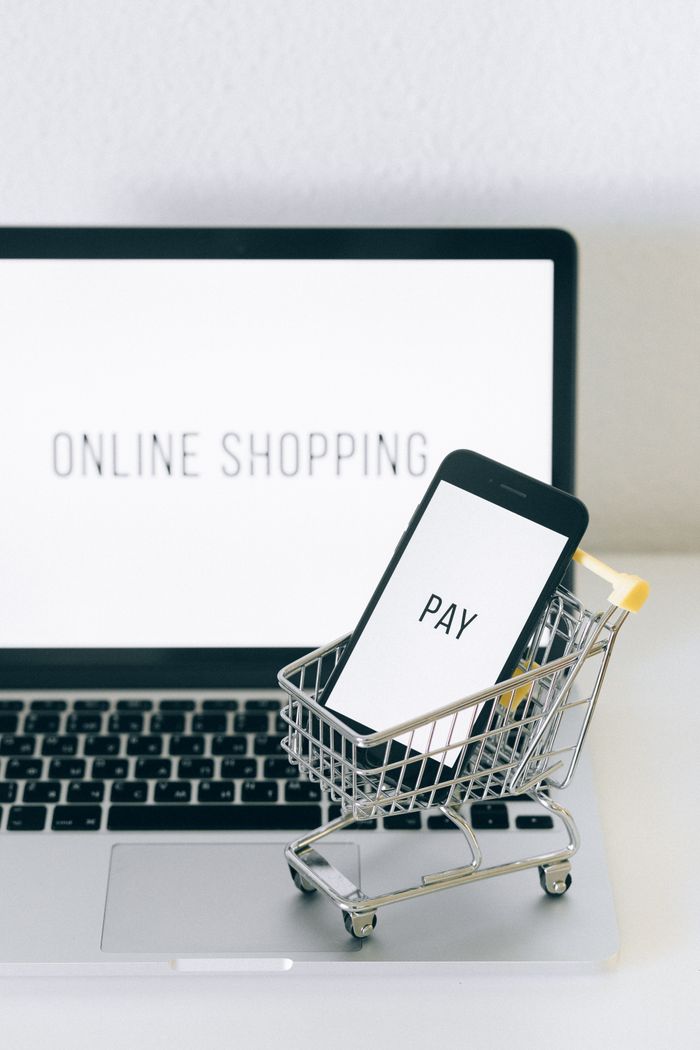 Un smartphone placé dans un mini chariot sur un ordinateur portable illustre le shopping en ligne et le paiement numérique.
